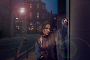 Image has a futuristic theme of dark blues, featuring a model in centre of image with lens flare from a street lamp in the background