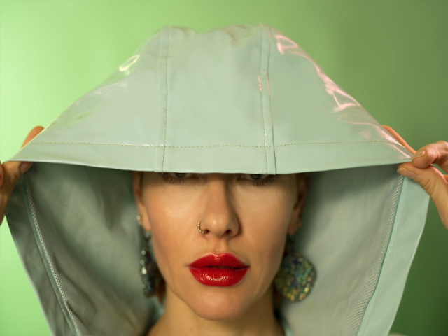 Image is green on green, featuring Liliya, a model with red/orange hair in a green mac covering her eyes against a green background