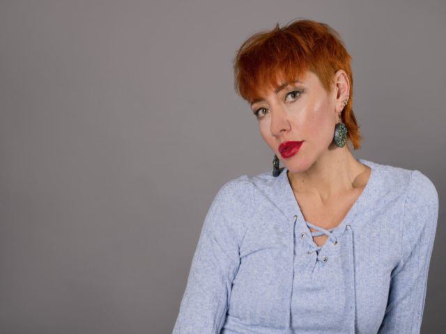 Image featuring Liliya, a model with red/orange hair wearing blue against a grey background