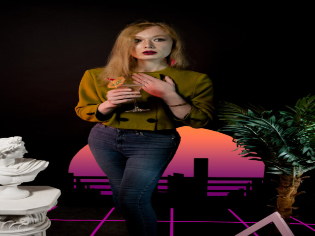 Model is standing, wearing a vintage chartreuse jacket and jeans, holding cocktail. To model's right is a marble bust on a plinth. To the model's left is a palm tree and top of a pink triangle. The background is black with a striated sun with a orange-purple gradient. The floor is black with a pink grid.