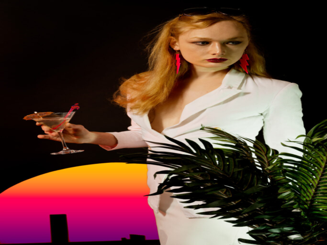 Featuring a model in white suit, holding a cocktail against a striated sun with a night cityscape. In foreground is a plant covering part of the model.
