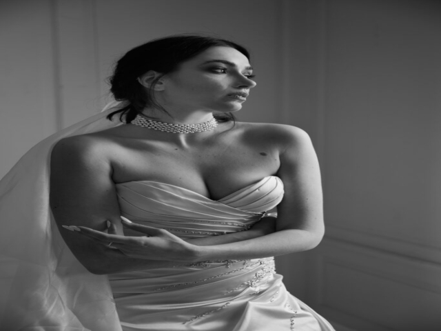 Black and white image of a female, caucasian model sat in wedding gown in a white studio, looking askance