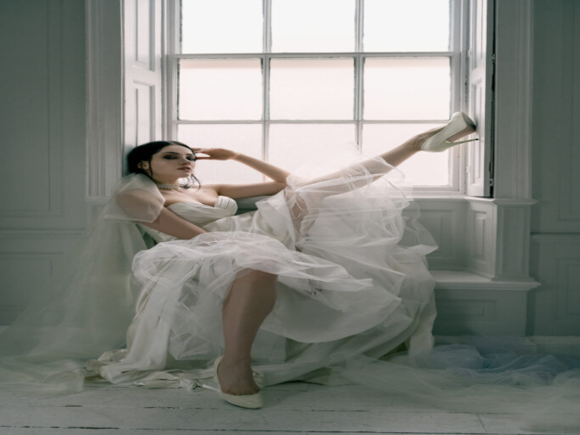 Caucasian model sat in wedding gown, in a white studio against a large window