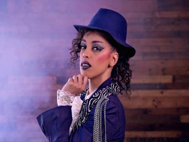 Image features a model in character as the musician Prince, looking at the camera