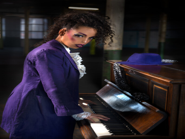 Image features a model in character as the musician Prince, playing an upright piano in a mill studio