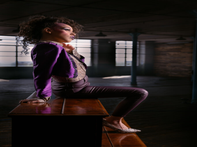 Image features a model in character as the musician Prince, sat on an upright piano in a mill studio