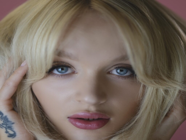 Headshot of Katey, blonde, female model with pink makeup on a pink background