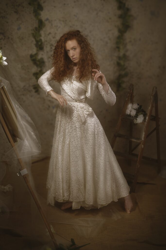 Image is a fine art image, featuring a Caucasian woman with red hair wearing a vintage lace wedding dress
