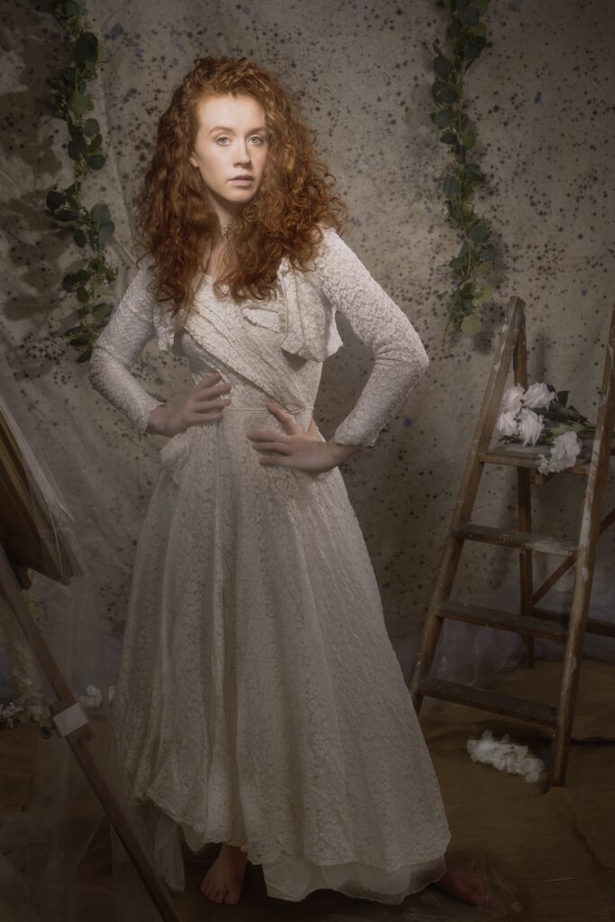 A fine art image, featuring a Caucasian woman with red hair wearing a vintage lace wedding dress