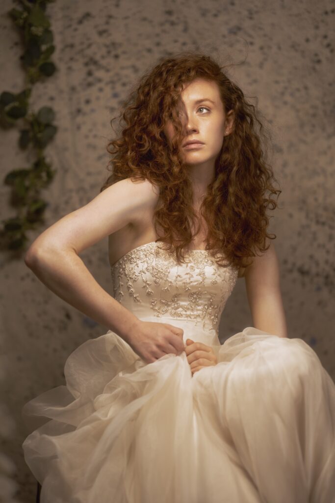 Image is a fine art image, featuring a Caucasian woman with red hair wearing a vintage wedding dress