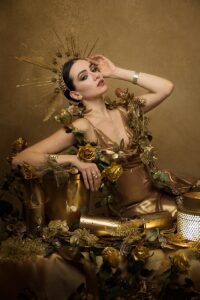 Image of a female model in a gold dress, surrounding by gold items