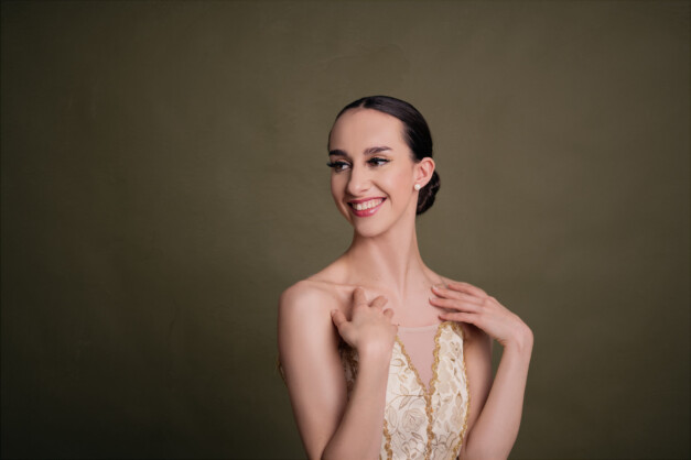 Image of Erica, a ballerina. A portrait of Erica, smiling in an ivory tutu with embroidered decorations.