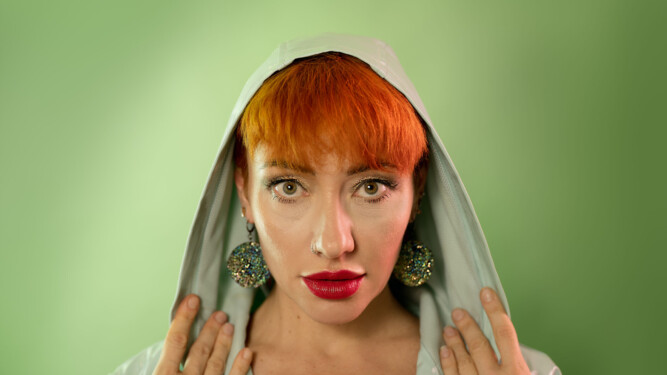 Image is green on green, featuring ahead and shoulders shot of Liliya, a model with red/orange hair in a green mac against a green background